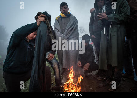 Essayez de réfugiés pour se réchauffer et sécher ils chiffons mouillés par le feu après une nuit de pluie au camp de réfugiés de fortune de l'Greek-Macedonian bord Banque D'Images