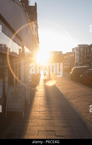 Anneau de lumière qui brille sur la chaussée par une route vers le bas d'une rue de Londres au coucher du soleil que les gens vaquent à leur vie quotidienne, London, Angleterre, Grande-Bretagne. Banque D'Images