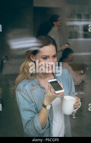 Female executive talking on mobile phone while having coffee Banque D'Images