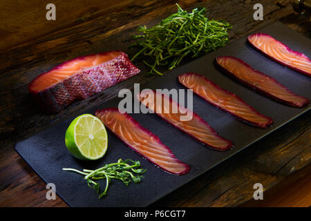 Filet de saumon en tranches, salés au jus de betteraves rouges, servis sur des feuilles de blé entier avec de la salade, du sel de mer et poivre sur surface métallique. Vue d'en haut. Banque D'Images