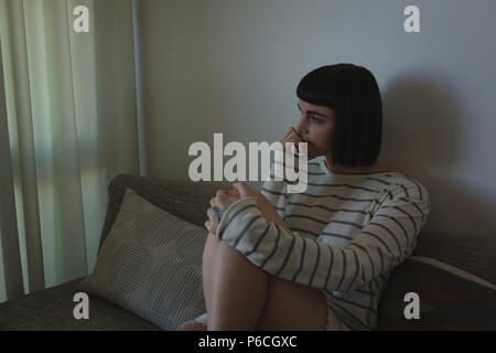 Worried woman sitting on sofa in living room Banque D'Images