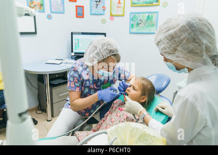 Enfant avec une mère à la réception d'un dentiste. La jeune fille se trouve dans le fauteuil, derrière sa mère. Le médecin travaille avec un assistant. Procédure de drillin Banque D'Images