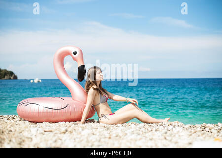 Jeune femme avec bandeau assis près de flamingo gonflés géant sur une plage avec de l'eau turquoise de la mer Ionienne l'Albanie Banque D'Images