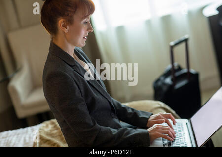 Businesswoman using laptop on bed Banque D'Images