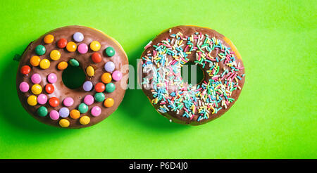 Concept des pâtisseries. Donuts avec lustre de chocolat, sprinkles, 2, vue d'en haut et isolé sur fond vert. Banque D'Images