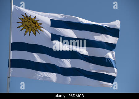 Brandir le drapeau uruguayen dans le vent sur fond de ciel bleu. Pays Uruguay mât avec emblème national. Banque D'Images