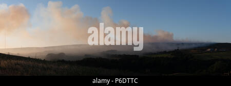 West Pennine Moors , Royaume-Uni, 29 juin 2018. Panorama montrant l'origine de l'incendie derrière une maison de ferme sur la colline d'hiver avec de la fumée qui balaye à l'hiver Hill television mast clairement visibles à travers la fumée des feux d'herbe à droite. Banque D'Images