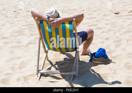 Bournemouth, Dorset, Royaume-Uni. 30 juin 2018. Météo au Royaume-Uni : la vague de chaleur se poursuit et une autre journée chaude et ensoleillée sur les plages de Bournemouth. Le milieu de la matinée et les plages se regorgent alors que les amateurs de soleil se dirigent vers le bord de mer. Une légère brise rend la chaleur plus supportable. Homme baignant le soleil assis dans une chaise longue. Banque D'Images