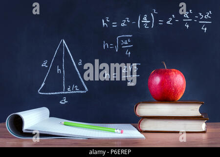 Livre vert sur Apple et stylo en bois ouverte sur l'ordinateur portable sur un bureau. Théorème de Pythagore écrit par la craie sur tableau noir. Classe de l'école et l'éducation Banque D'Images