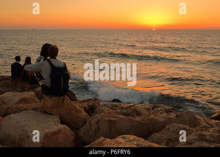 Coucher de soleil romantique sur la mer, deux couples s'asseoir sur les rochers du littoral et profiter du coucher du soleil Banque D'Images