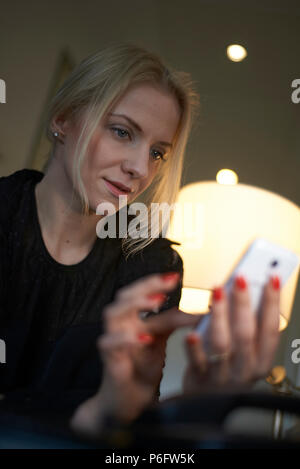 Une jeune femme de race blanche assis à un bureau dans sa chambre d'hôtel à l'aide de son téléphone portable pour prendre rendez-vous Banque D'Images