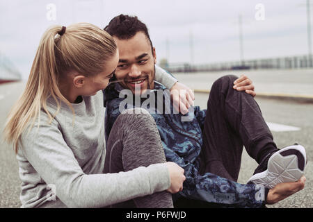 Young couple in sportswear assis sur un chemin ensemble en faisant une pause à partir d'une exécution sur un jour nuageux Banque D'Images
