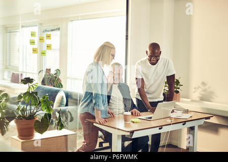 Groupe diversifié de smiling business colleagues discussing un projet ensemble tout en travaillant à un bureau à l'intérieur d'un bureau en verre Banque D'Images