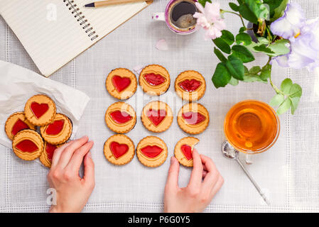 Les mains des femmes jouer tic tac toe jeu par les cookies avec des cœurs et baiser sur le tableau blanc avec plateau et tasse à café, ordinateur portable et de fleurs fraîches. Concept d'amour Banque D'Images