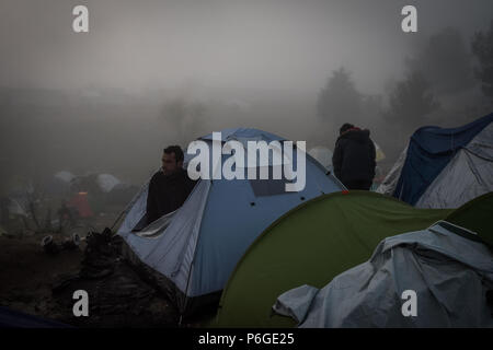 Un homme regarde des réfugiés à partir d'une tente lors d'un matin brumeux sur le camp de fortune de l'Greek-Macedonian frontière près du village grec de Idomeni. Banque D'Images