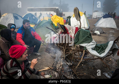 Essayez de réfugiés pour se réchauffer et sécher ils chiffons mouillés par le feu après une nuit de pluie au camp de réfugiés de fortune de l'Greek-Macedonian bord Banque D'Images