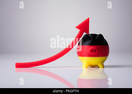 Close-up of Piggybank peint avec drapeau allemand et Flèche Rouge montrant vers le haut Banque D'Images