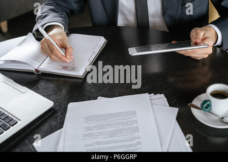 Businessman on business lunch au restaurant sitting at table close-up holding digital tablet taking notes in planner Banque D'Images