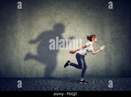 Femme courir loin de son ombre sur le mur de graisse. Contrôle de poids concept Banque D'Images