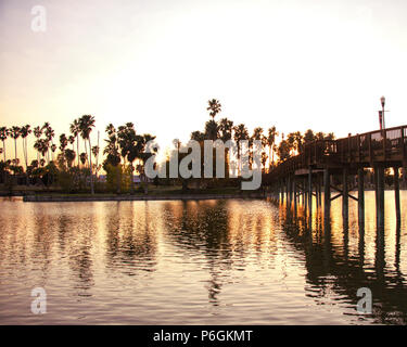 Le coucher du soleil tombant sur palmiers entourée par un lac et pont. Banque D'Images