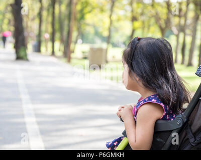 Petite fille asiatique assis dans une poussette au parc public. Elle attends avec impatience Banque D'Images