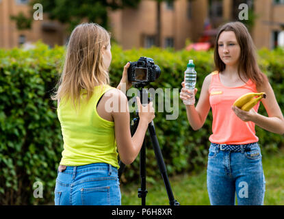 L'été dans la nature girl écolière. Écrit la vidéo à l'appareil photo. Dans ses mains tient une bouteille d'eau et les bananes. Le concept d'une saine alimentation. Banque D'Images