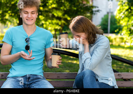 Un gars avec une fille à l'été dans un parc de la nature. Raconte une blague drôle. La jeune fille rit émotionnel avec sa main sur sa bouche. 23-08-2003 Les élèves heureux Banque D'Images