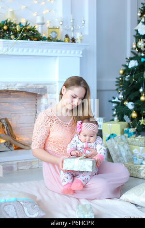 Young caucasian mère petite fille de don présent près de cheminée décorée et l'arbre de Noël. Banque D'Images