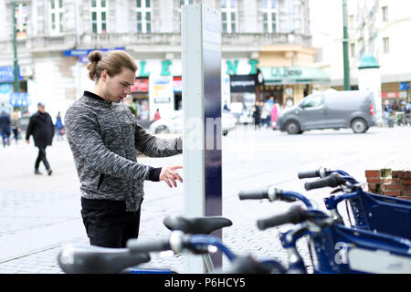 Jeune homme en vélo, avec l'embauche de la machine en ville, route et trafic piétons en arrière-plan. Banque D'Images