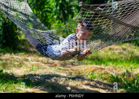 Joyeux garçon couché sur le hamac dans le jardin. Banque D'Images