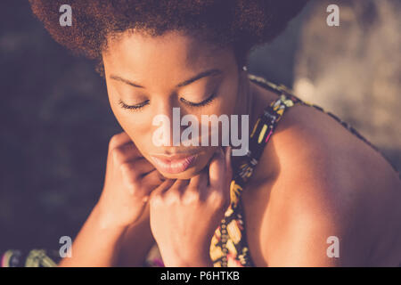 Belle race noir style de cheveux afro africaine modèle avec les yeux fermés et la main sur le visage poser sous le soleil. concept de beauté pour la peau noire et à Banque D'Images