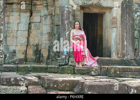 Angkor, Cambodge - Nov 17, 2017 : petite fille cambodgienne en costume traditionnel assis à l'entrée du temple Bayon. C'est richement décorée à un temple Khmer Banque D'Images