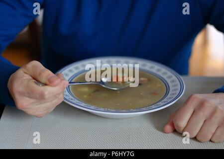 Seul l'homme est assis à table et mange de la soupe, de la soupe avec la plaque sur la table, l'homme en pull bleu Banque D'Images