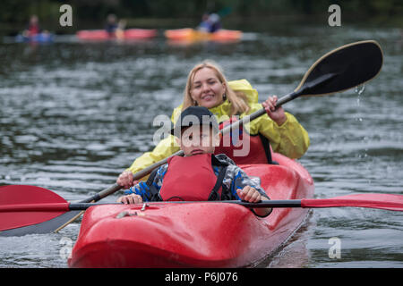 Adolescents avec une expression du visage frustré se trouve dans un bateau de sport kayak avec une mère dans l'arrière-plan qui est amusant de rangée Banque D'Images