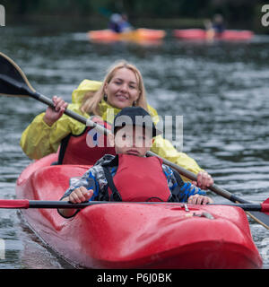 Adolescents avec une expression du visage frustré se trouve dans un bateau de sport kayak avec une mère dans l'arrière-plan qui est amusant de rangée Banque D'Images