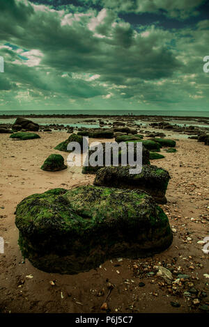 Image d'Old Hunstanton Beach avec un moody sky et des roches couvertes d'algues dans l'avant-plan. Banque D'Images