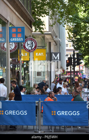 Les gens s'assoient à l'extérieur d'une rangée de cafés et des plats à emporter commerces, y compris le fabricant de sandwich et de boulangerie Greggs, Mikel le café et manger. sur Tottenham Court Road i Banque D'Images