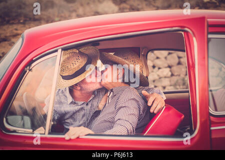 Couple de personnes âgées avec chapeau, avec des lunettes, avec des cheveux gris et blanc, avec chemise décontractée, sur vintage voiture rouge en vacances profiter du temps et de la vie. Avec un chee Banque D'Images