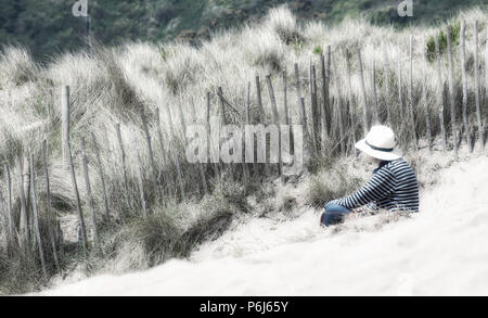Femme assise sur la plage, dans un chapeau Banque D'Images