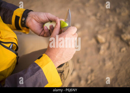 Close up de la main de l'un coupe la pomme verte avec un couteau au cours d'une aventure de plein air outdoor trekking dans le désert. explorer le monde et d'obtenir une Banque D'Images