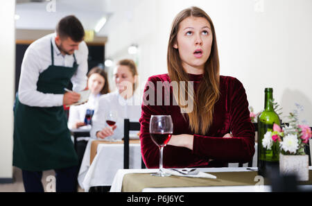 Femme élégante en colère s'attend à ce que l'homme pour le dîner dans le restaurant de luxe intérieur. Banque D'Images