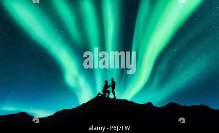 Northern Lights et silhouettes d'un homme faire de demande en mariage à sa petite amie sur la colline. Paysage avec un ciel étoilé de nuit, aurora borealis, cou Banque D'Images