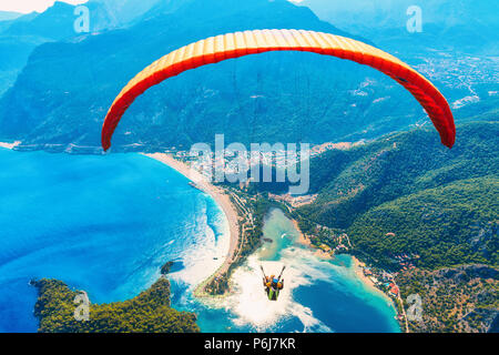 Parachute dans le ciel. Tandem parapente voler au-dessus de la mer avec de l'eau bleue et les montagnes en journée ensoleillée. Vue aérienne de la bleue et de parapente Banque D'Images