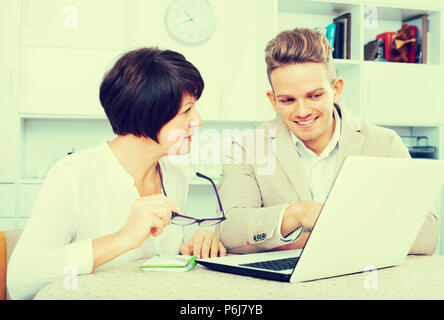 Maman mature et fils d'examiner de nouveaux logiciels sur laptop sitting at table Banque D'Images