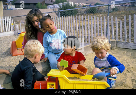 Enfants jouant dans le sable fort comme jeune femme supervise  <R. © Myrleen Pearson Banque D'Images