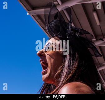 Une femelle race goer portant des lunettes et fascinator cris et sourit à l'enthousiasme que son cheval gagne à l'hippodrome de York, York, Angleterre, le 30 juin 2018 Banque D'Images