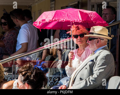 Une dame et un monsieur à l'abri du soleil à l''hippodrome de York, tenant un parapluie rose, York, Angleterre, le 30 juin 2018 Banque D'Images