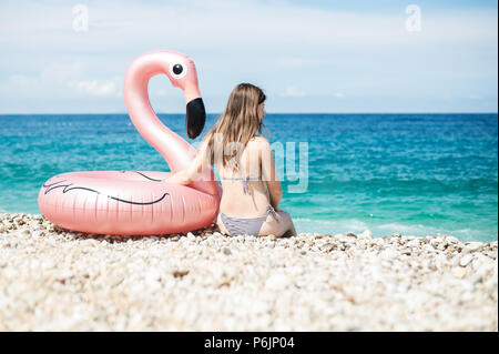 Jeune femme avec bandeau assis près de flamingo gonflés géant sur une plage avec de l'eau turquoise de la mer Ionienne l'Albanie Banque D'Images