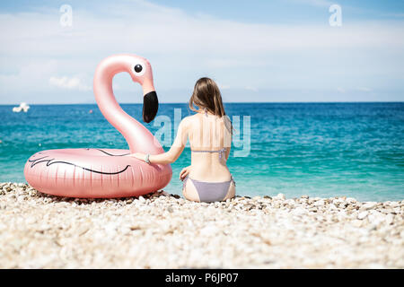 Jeune femme avec bandeau assis près de flamingo gonflés géant sur une plage avec de l'eau turquoise de la mer Ionienne l'Albanie Banque D'Images