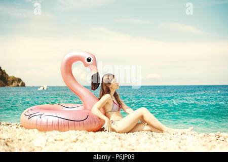 Jeune femme avec bandeau assis près de flamingo gonflés géant sur une plage avec de l'eau turquoise de la mer Ionienne l'Albanie Banque D'Images